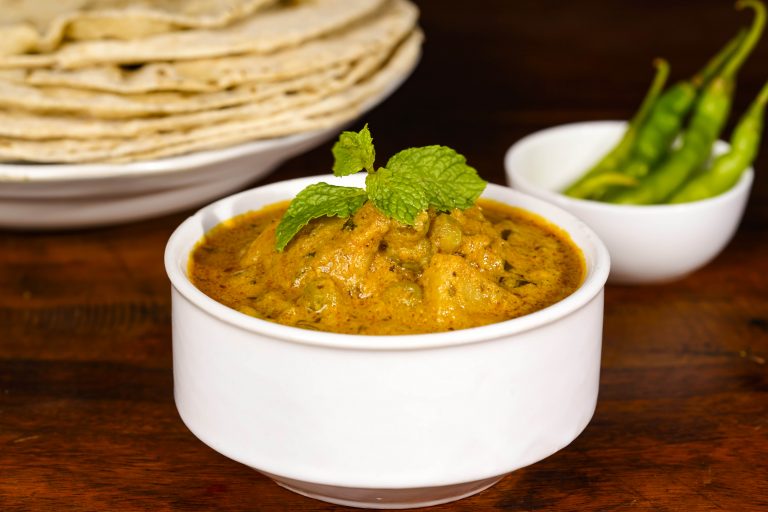 A stack of rotis with a bowl of veg curry and green chillies