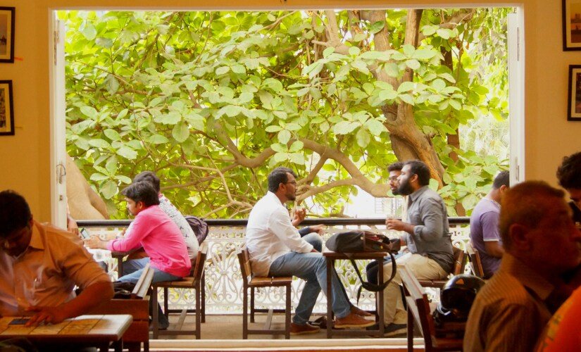 People at the canteen tables, with big trees outside the open windows