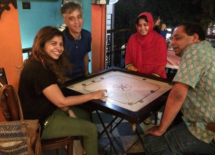 Four people round a carrom board, laughing
