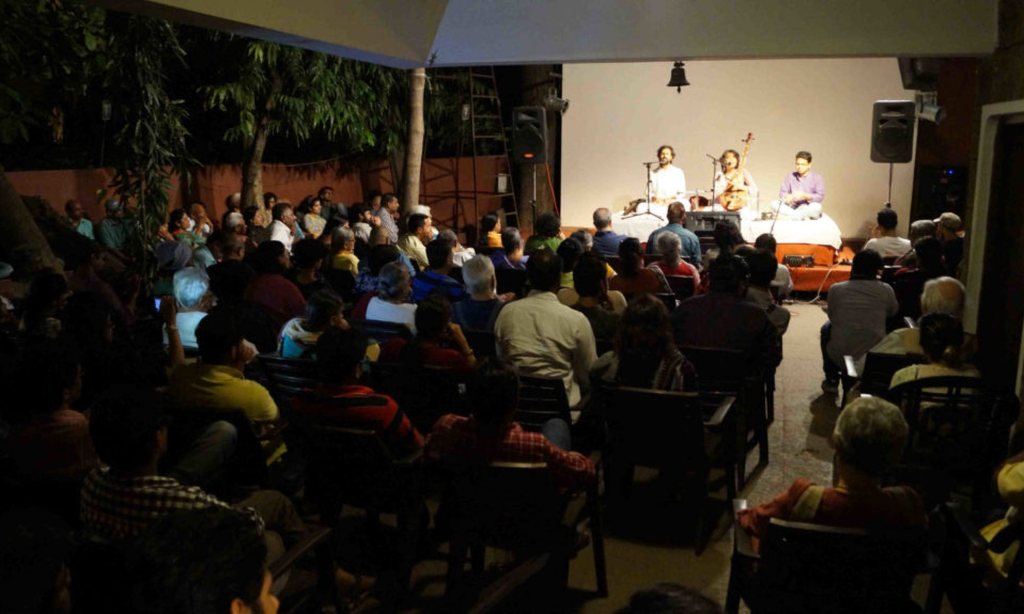 A packed audience at night facing musicians on a lit stage